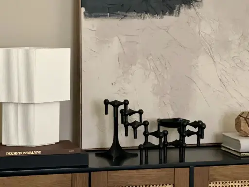 En stilren stilleben inredning med en vit lampa, svarta ljusstakar och en bok med texten "Dior".
