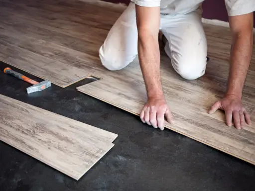 Pose de parquet flottant : un artisan installe des lames de bois sur un sol noir. Le prix de pose est une préoccupation pour ce type de revêtement.