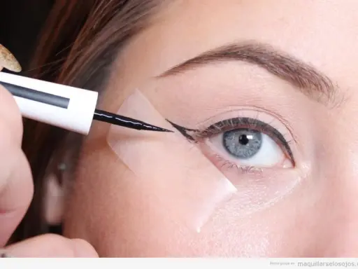 Aplicando delineador con cinta para aprender como hacer la raya del ojo para principiantes. Ojo azul, ceja definida, delineador negro.
