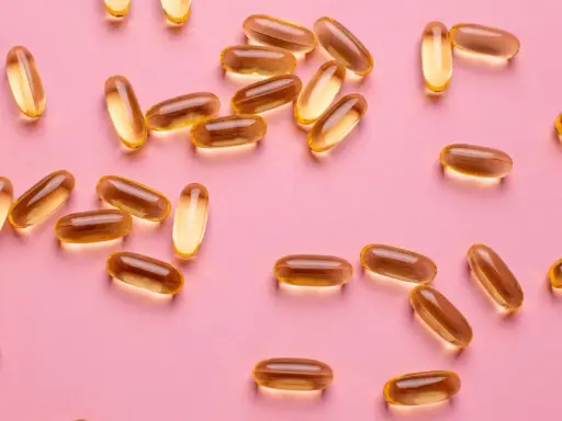 Capsule dorate sparse su sfondo rosa, utili per la vitamina D in gravidanza.