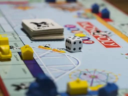 Kostka i pionki na planszy Monopoly. Gra planszowa uczy strategii, negocjacji i zarządzania finansami, realizując cele i zadania.
