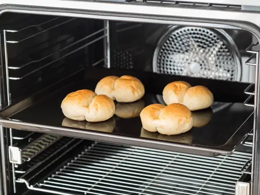 Cinq petits pains dorés sur une plaque de cuisson dans un four. C'est une bonne question : qu'est-ce qu'un lèchefrite ? C'est cette plaque !