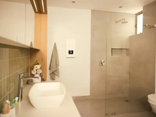 Modernes Bad mit Dusche und Waschbecken. Ein Durchlauferhitzer hängt an der Wand, der für warmes Wasser sorgt, auch wenn man ihn an 230V anschließen möchte.