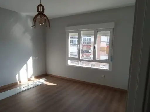 Habitación con suelo de madera, paredes grises y ventana. El sol ilumina la estancia, sugiriendo un buen **precio medio reforma integral**.