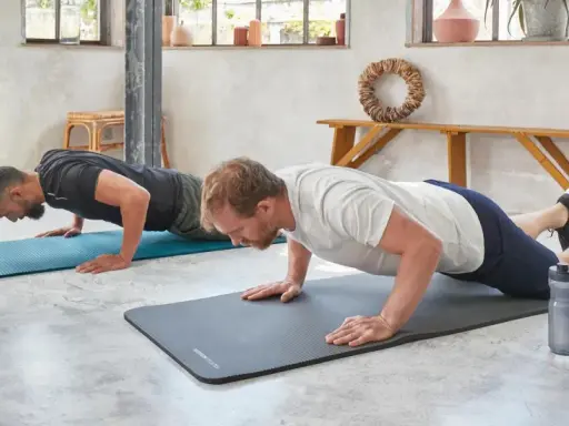 Dwóch mężczyzn wykonuje ćwiczenia na triceps w domu, robiąc pompki na matach.