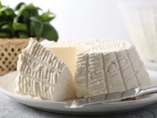 Un morceau de ricotta fraîche sur une assiette, avec des herbes en arrière-plan. Idéal pour connaître les calories de la ricotta.