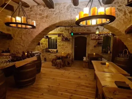 Intérieur d'une taverne médiévale avec murs en pierre, tables en bois et chandeliers. Le tavernier moyen âge y servirait sûrement de l'hydromel.