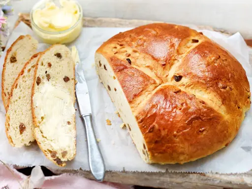 Ein goldbraunes Osterbrot mit Rosinen, aufgeschnitten und mit Butter bestrichen. Perfekt für ein Osterbrot Rezept.
