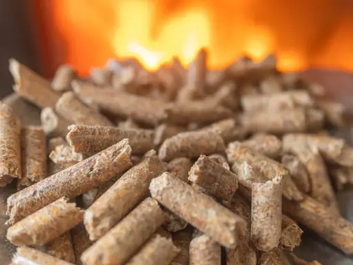 Granulés de bois prêts pour l'installation d'un poêle à granule, avec des flammes chaudes en arrière-plan.