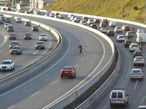Tráfico intenso en una autopista con varios carriles. Coches, furgonetas y una moto forman la **circulación vao** en un día soleado.