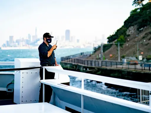 Un homme sur un bateau utilise une radio. Il est en communication, peut-être sur une fréquence vhf libre, avec la ville en arrière-plan.