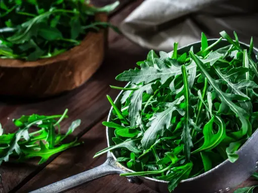 Frischer Rucola in einem Sieb, bereit für eine gesunde Mahlzeit. Daneben ein Holzschälchen mit mehr Rucola.