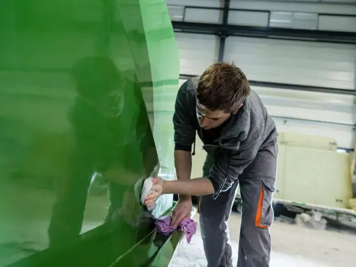 Un ouvrier polit la coque d'un bateau en polyester vert vif dans un atelier.