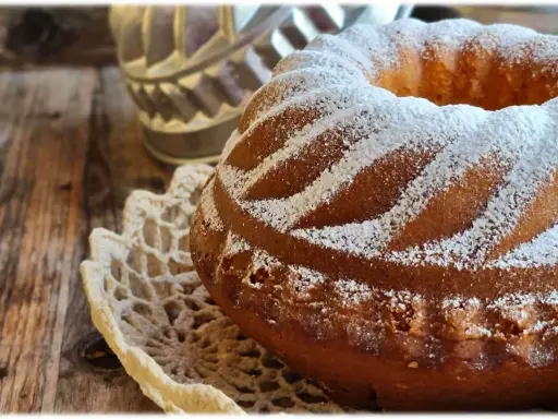Ciambellone allo yogurt soffice e profumato, cosparso di zucchero a velo su un centrino di pizzo, pronto per essere gustato.