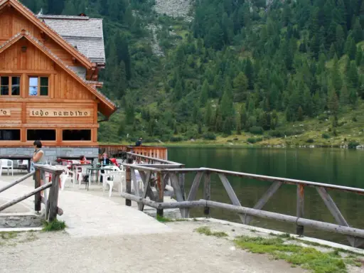 Rifugio sul lago nambino, con tavoli all'aperto e un bosco di conifere sullo sfondo.
