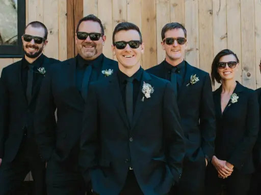 Groomsmen in matching black suits and sunglasses, showcasing stylish black suit ideas for a wedding party.