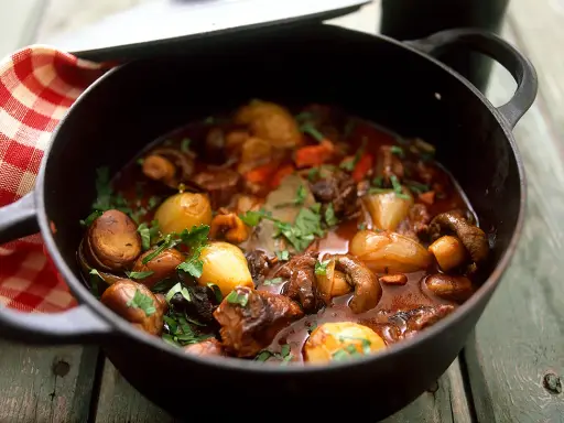 En mustig boeuf bourguignon i gjutjärnsgryta med champinjoner, lök och örter.