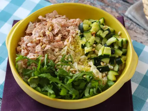 En gul skål med ris, lax, gurka och ruccola. En hälsosam och färgstark måltid.