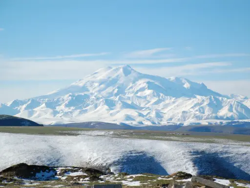 Pokryty śniegiem najwyższy masyw Wielkiego Kaukazu, Elbrus, góruje nad ośnieżonymi wzgórzami i zielonymi dolinami.