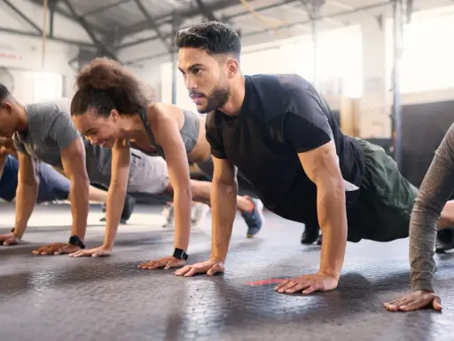Gruppe trainiert Liegestütze im Fitnessstudio. Ein Mann mit Bart konzentriert sich auf sein ganzheitliches Training.
