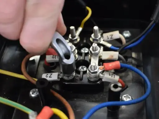 Main d'un technicien manipulant un connecteur sur un bornier électrique. Le moteur électrique chauffe et s'arrête, nécessitant une vérification des connexions.