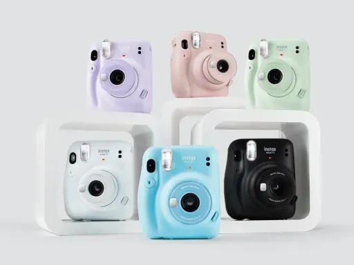 Pięć aparatów Instax Mini 11 w różnych kolorach: fioletowym, różowym, zielonym, białym, niebieskim i czarnym.