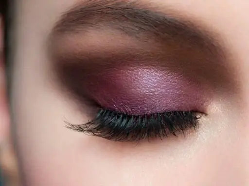 Maquillaje de ojos con sombra morada brillante y pestañas largas, ideal para realzar la mirada en párpados caídos.