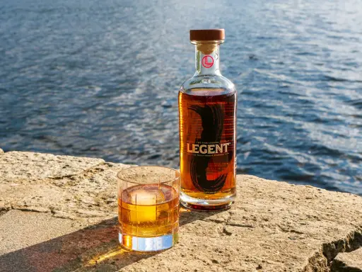 Legent Bourbon Whisky: Ein Glas und eine Flasche stehen auf einem Stein am Wasser. Was ist Bourbon Whisky? Ein Genuss für besondere Momente.