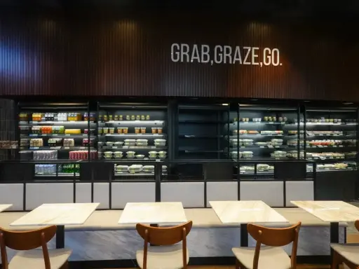Refrigeradores llenos de comidas listas para llevar. El letrero "GRAB, GRAZE, GO" inspira una comida rápida y deliciosa.