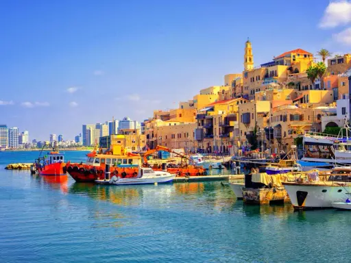 Bunte Boote im Hafen von Tel Aviv, mit der historischen Altstadt im Hintergrund und modernen Hochhäusern am Horizont.