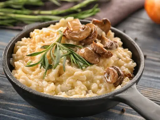 Cremoso arroz redondo risotto con champiñones salteados y romero fresco en sartén de hierro fundido.