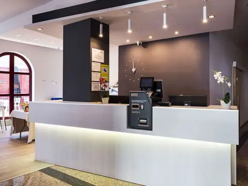 Recepción moderna y luminosa de la residencia Nuevo Versalles, con mostrador blanco, pantalla y máquina de efectivo.
