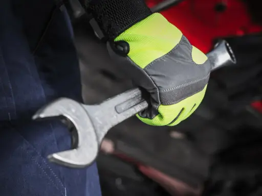 Mano con guante de alta visibilidad, parte de material de protección laboral, sujetando una llave inglesa.