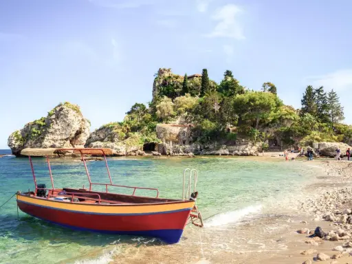Ein Boot liegt im kristallklaren Wasser vor einer felsigen Insel mit üppiger Vegetation. Das sizilien wetter im oktober ist perfekt für einen entspannten Tag am Strand.