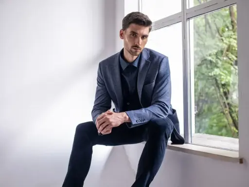 Elegancki mężczyzna w granatowej koszuli i marynarce, zastanawia się, jakie spodnie do niebieskiej koszuli będą najlepsze.