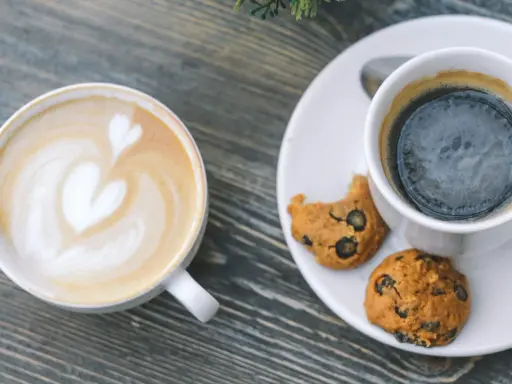Zwei Tassen Kaffee: ein Latte mit Herz und ein starker Americano mit Keksen.