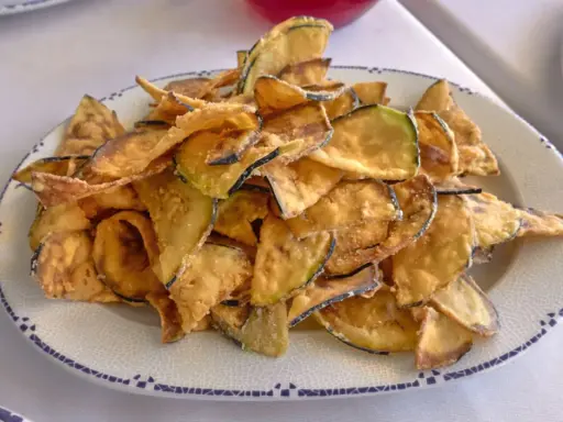 Montón de berenjenas fritas crujientes y doradas en un plato blanco con borde azul. ¡Un aperitivo delicioso!