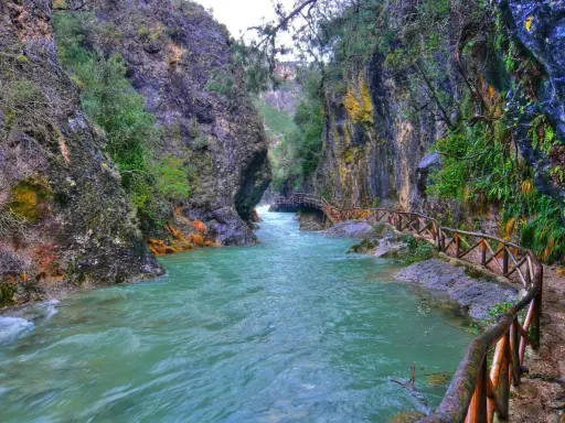 Un río turquesa serpentea entre cañones rocosos, con un sendero de madera que acompaña el recorrido. Ideales para rutas senderismo Jaén.