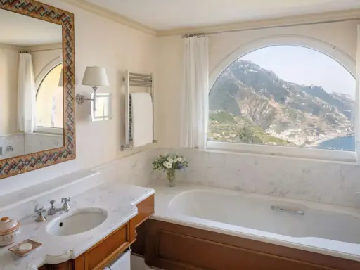 Un bagno di lusso con vasca, lavandino e specchio decorato, che offre una vista mozzafiato sulle montagne e sul mare. Tra i bagni più belli ed eleganti.