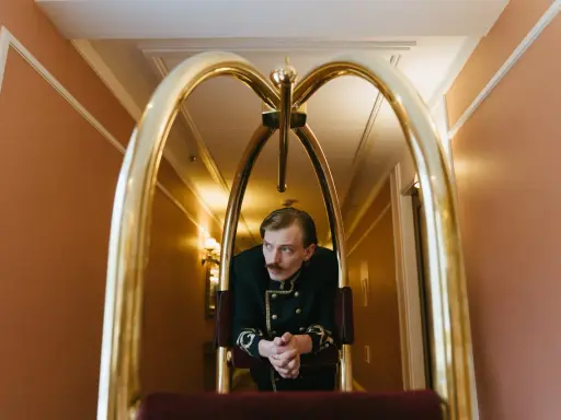 Elegancki hotelarz w historycznym mundurze czeka przy wózku bagażowym w hotelowym korytarzu.