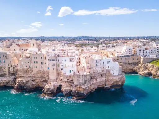 Vista aerea di Polignano a Mare, una delle più belle città da visitare in Puglia, con case bianche aggrappate alle scogliere a picco sul mare turchese.