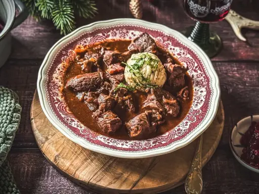 Ein festliches Hirschgulasch, wie es ein Sternekoch zubereiten würde, serviert mit Klößen und Preiselbeeren.