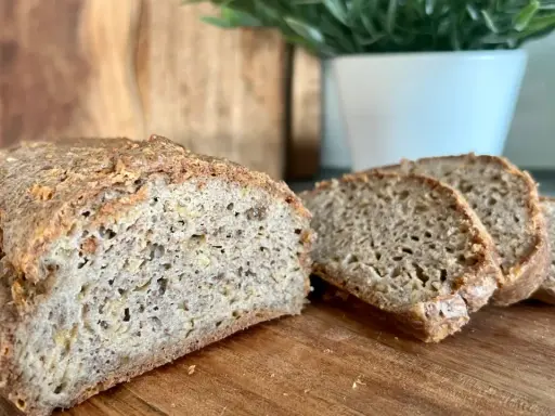 Chleb keto przepis. Domowy, puszysty bochenek z chrupiącą skórką, pokrojony na kromki, leży na desce.