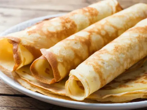 Gestapelte, gerollte Pfannkuchen ohne Mehl auf einem Teller. Sie sind goldbraun und sehen lecker aus.