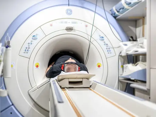 Mężczyzna leży w aparacie do rezonansu magnetycznego, przygotowując się do badania. Jego głowa jest uniesiona na poduszce, a uszy chronią słuchawki. To badanie może pomóc zrozumieć rezonans morficzny.