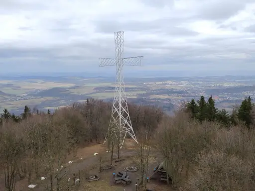 Wielki metalowy krzyż góruje nad lasem na Chełmcu. W dole rozciąga się panorama miasta i pagórkowatego krajobrazu.