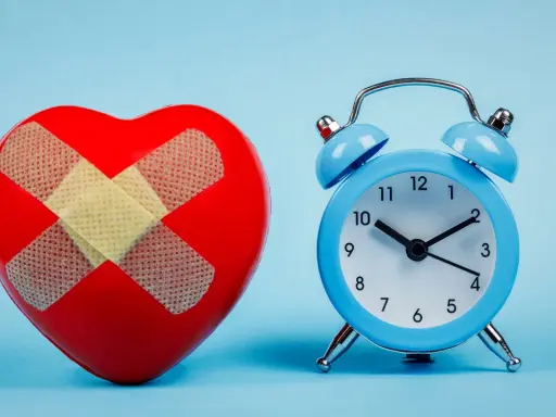 Rotes Herz mit Pflastern und blauer Wecker. Wenn du eine schlaflose Nacht hast, was tun? Zeit für Heilung.