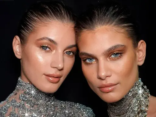 Dos mujeres con maquillaje dorado y un sutil rabillo del ojo, luciendo collares brillantes.