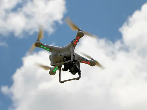 Weiße Drohne mit roten und grünen Lichtern fliegt im blauen Himmel mit Wolken. Beachten Sie die Drohnen Richtlinien für sicheren Flug.