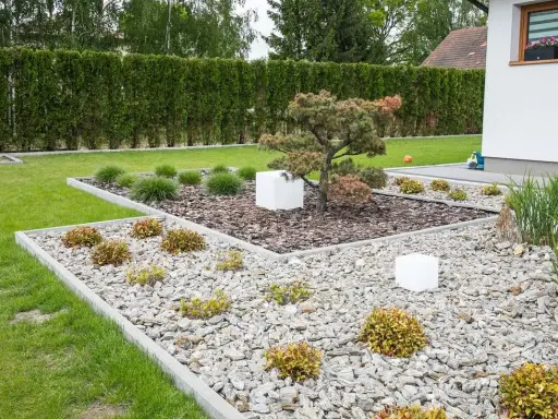 Nowoczesne klomby w ogrodzie galeria: kamień, kora, trawy ozdobne i miniaturowa sosna tworzą minimalistyczną kompozycję.